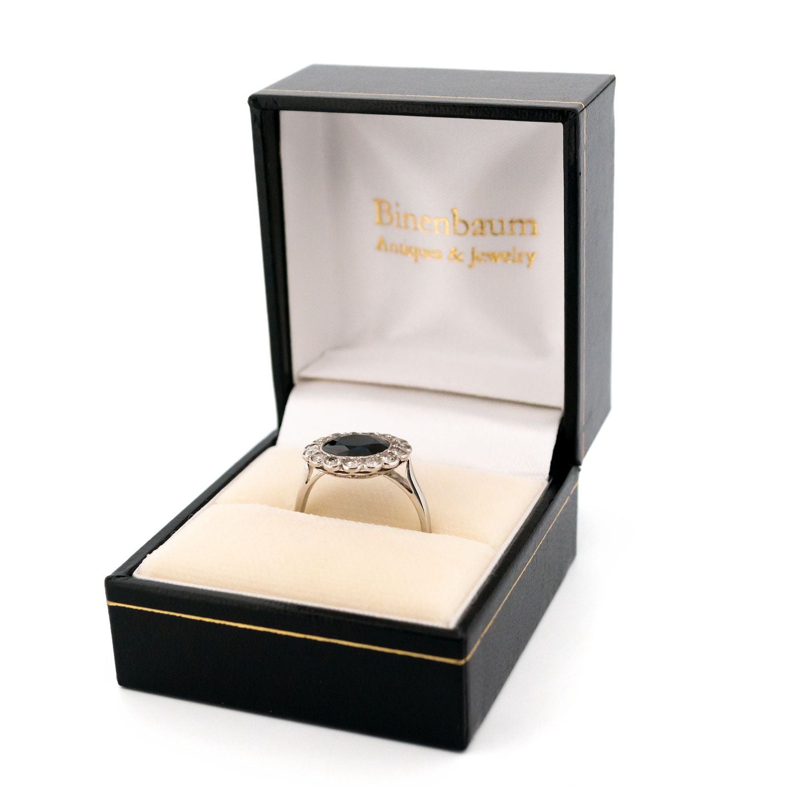 A flower shaped cluster ring set with a central sapphire surrounded by a halo of round diamonds, in platinum, in a ring box