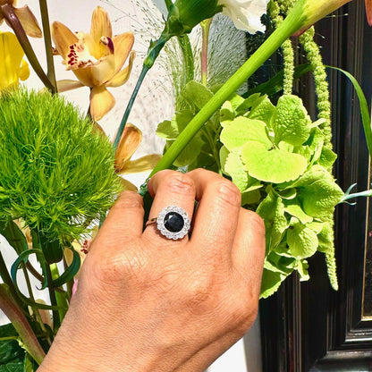 A flower shaped cluster ring set with a central sapphire surrounded by a halo of round diamonds, in platinum, modelled on a hand