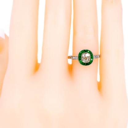 An emerald and diamond halo target cluster ring in platinum, modelled on a plastic hand
