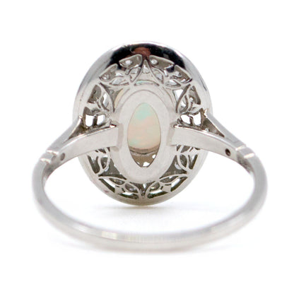 An oval shaped openwork ring with an opal centre and diamonds in swirl settings, in platinum