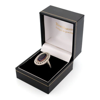 An oval shaped cluster ring with an amethyst centre and diamond surround, in platinum, in a ring box