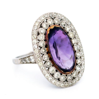 An oval shaped cluster ring with an amethyst centre and diamond surround, in platinum