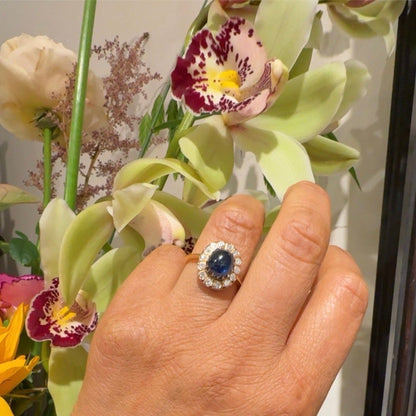 An oval cluster ring with a cabochon sapphire and diamond surround, in yellow gold, modelled on a hand