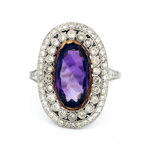 An oval shaped cluster ring with an amethyst centre and diamond surround, in platinum