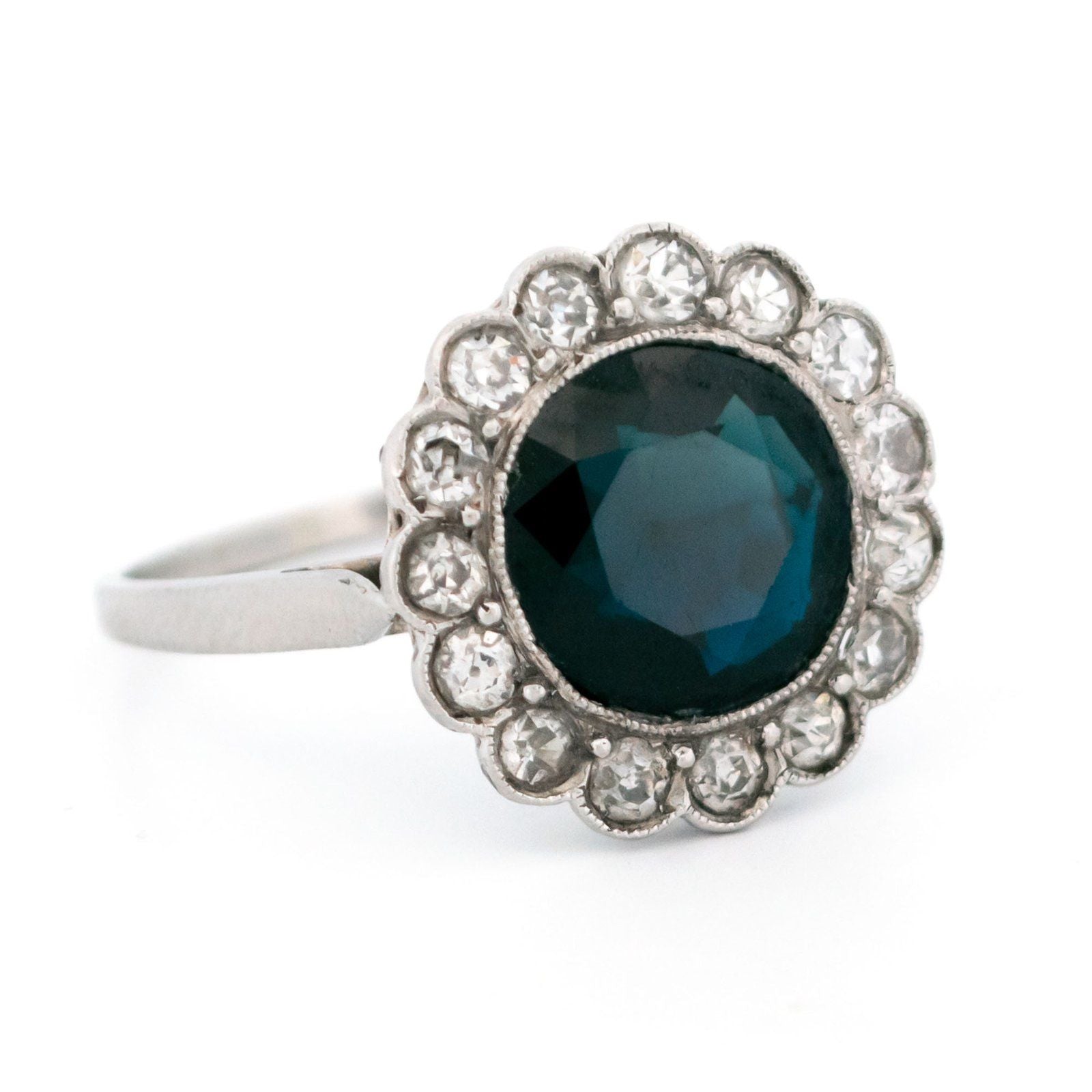 A flower shaped cluster ring set with a central sapphire surrounded by a halo of round diamonds, in platinum