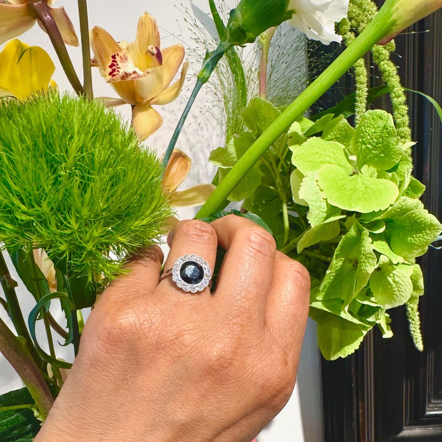 A flower shaped cluster ring set with a central sapphire surrounded by a halo of round diamonds, in platinum, modelled on a hand