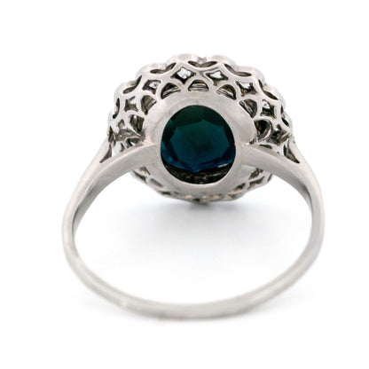 A flower shaped cluster ring set with a central sapphire surrounded by a halo of round diamonds, in platinum