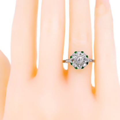 A diamond and emerald daisy cluster ring in platinum, modelled on a plastic hand