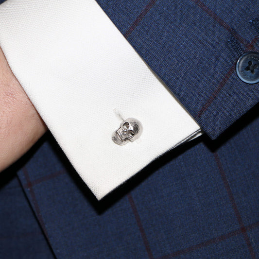 Close-up of a white gold skull cufflink in a white shirt cuff, against a blue suit
