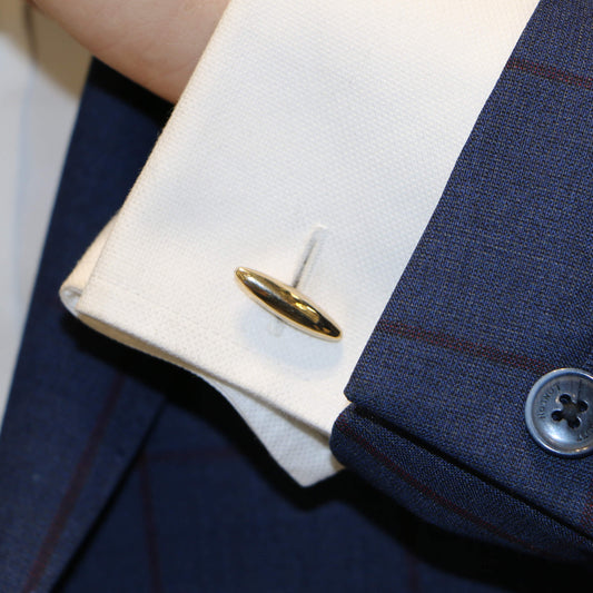 A torpedo shaped cufflink in a white shirt cuff against a blue suit