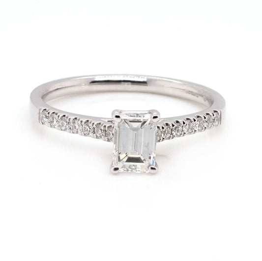 An emerald cut diamond ring in white gold, with diamond set shoulders