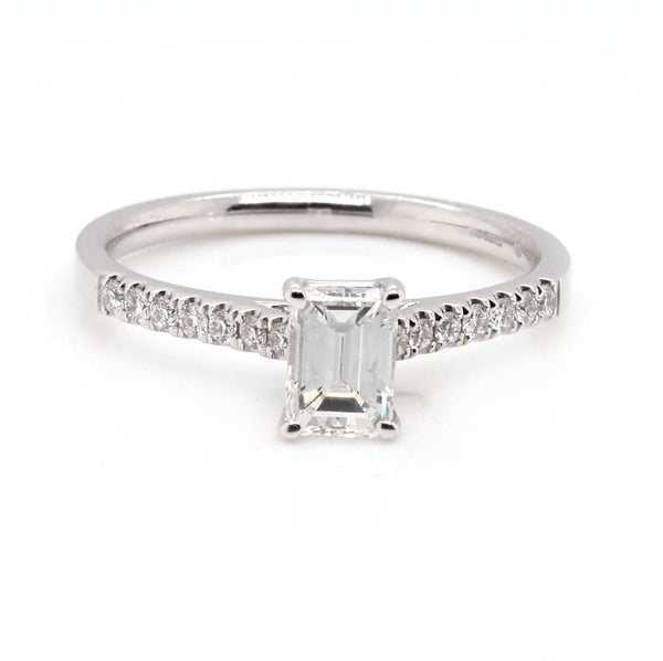 An emerald cut diamond ring in white gold, with diamond set shoulders