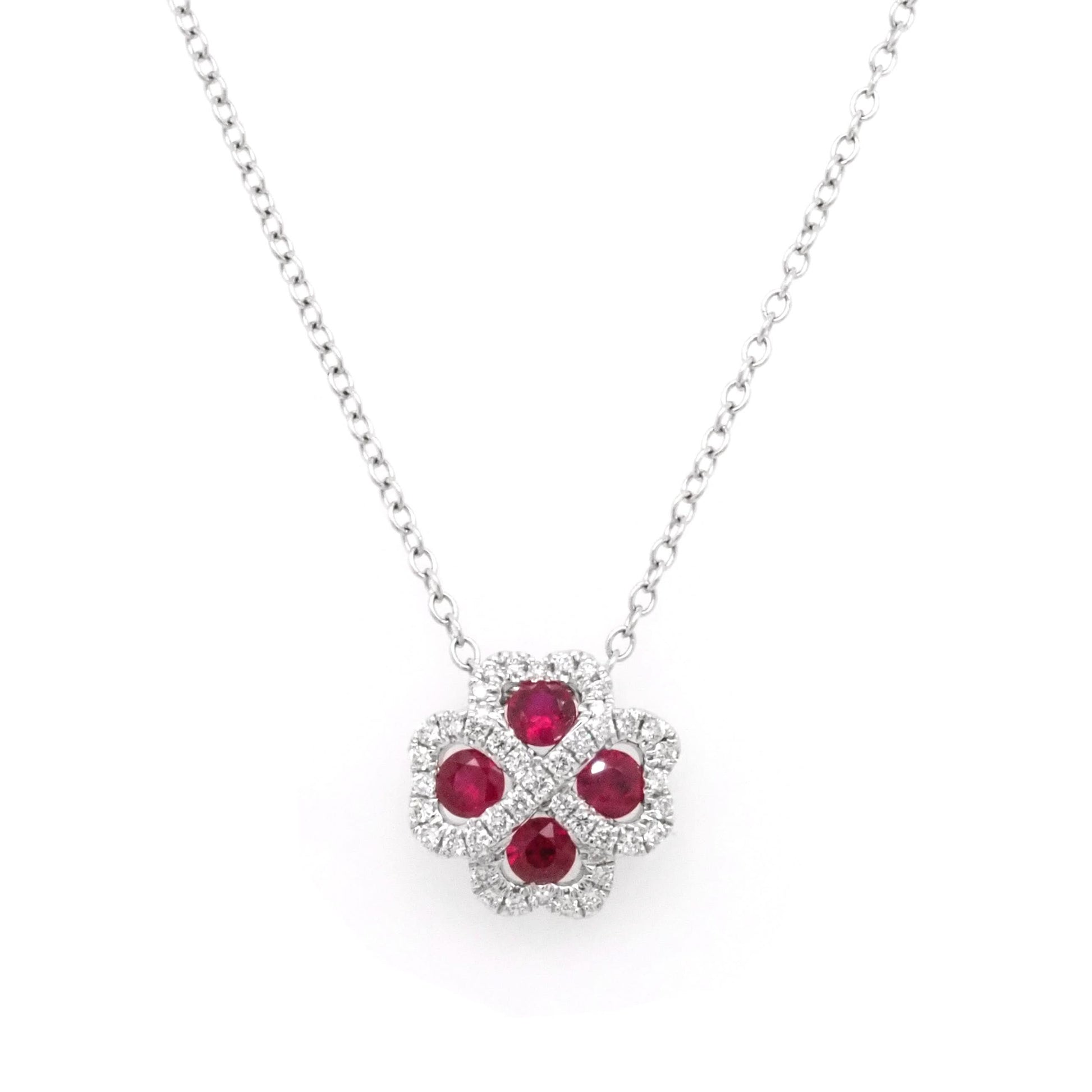 A white gold pendant necklace, the pendant a four leaf clover shaped cluster of rubies and diamonds, on an integrated chain