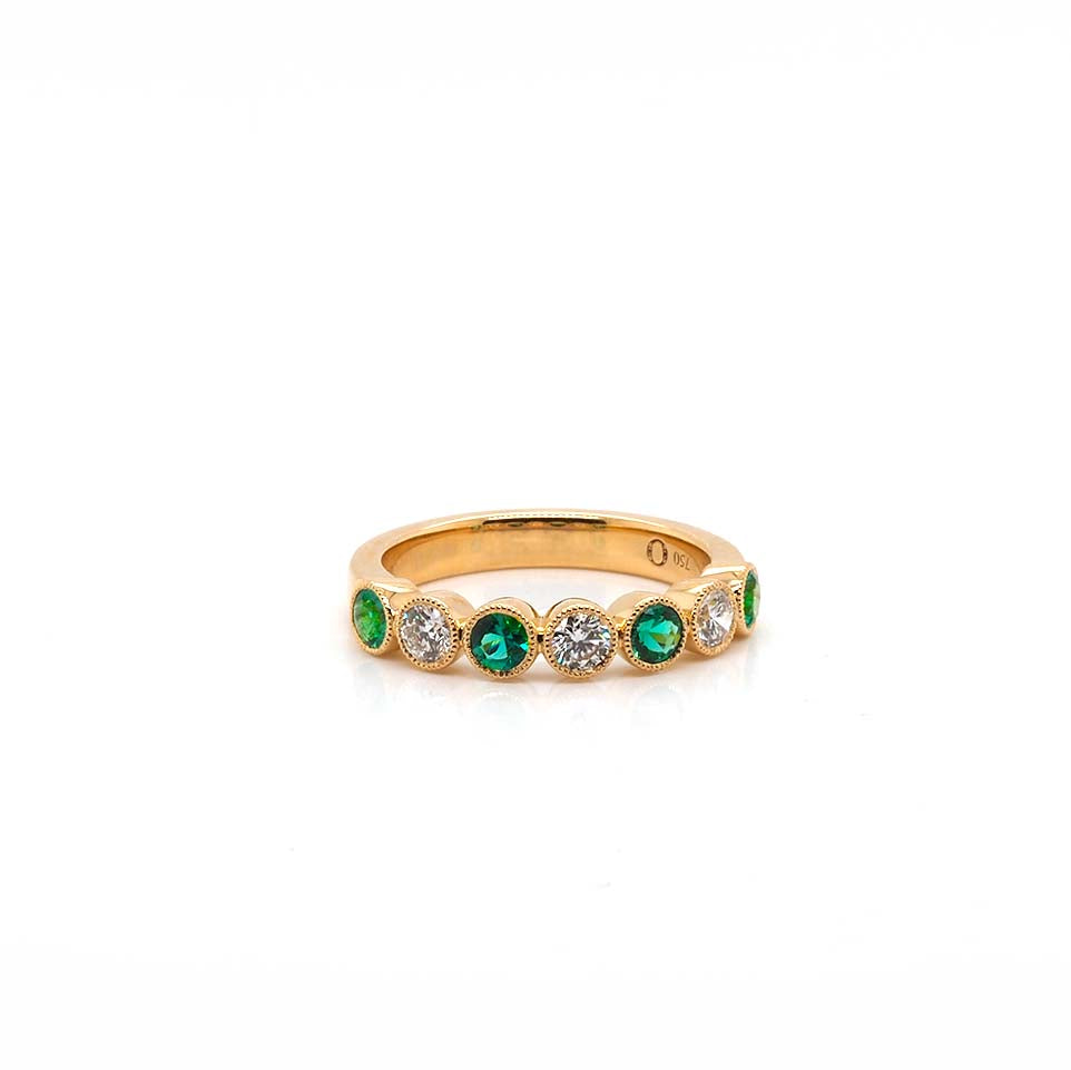 An emerald and diamond seven stone bezel set band ring in yellow gold