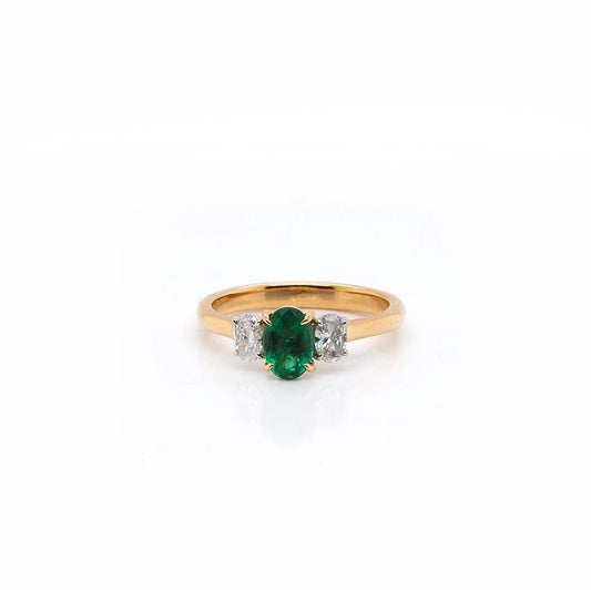 A three stone ring with an oval emerald centre and oval diamond shoulders, mounted in yellow and white gold