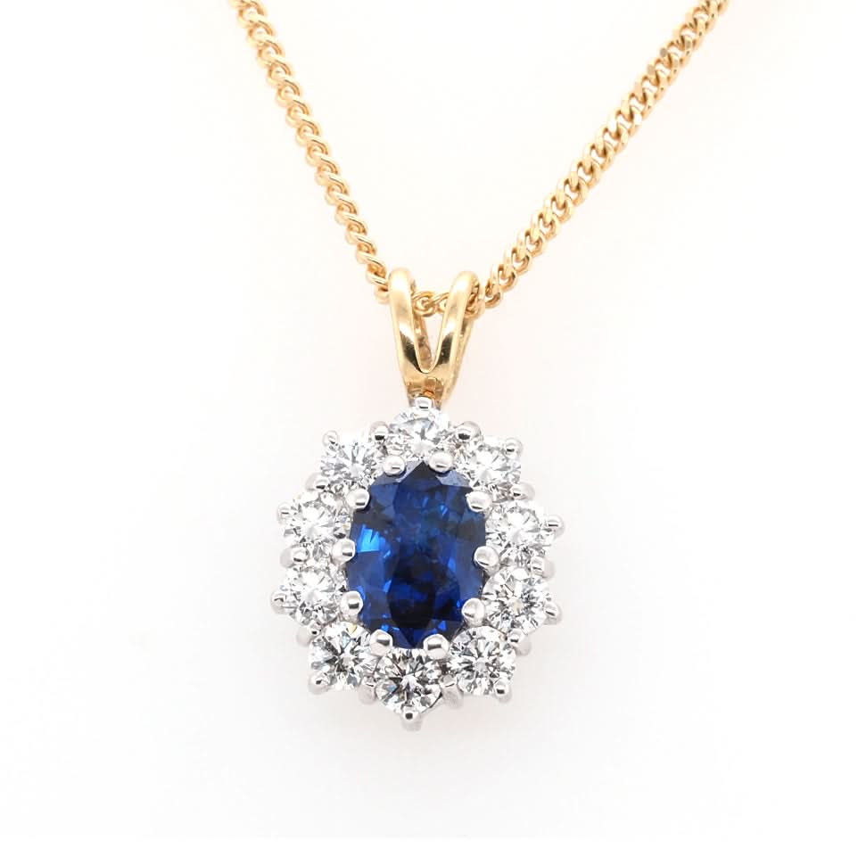 An oval cluster pendant with an oval sapphire and a diamond surround, in yellow and white gold, with a yellow gold chain