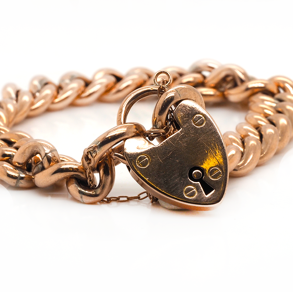 A rose gold curb link bracelet with a heart shaped padlock clasp