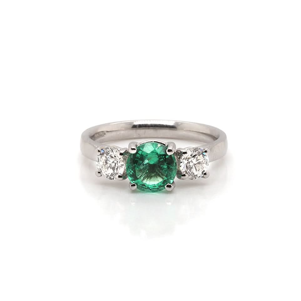 A three stone ring set with an emerald and two diamonds, in platinum