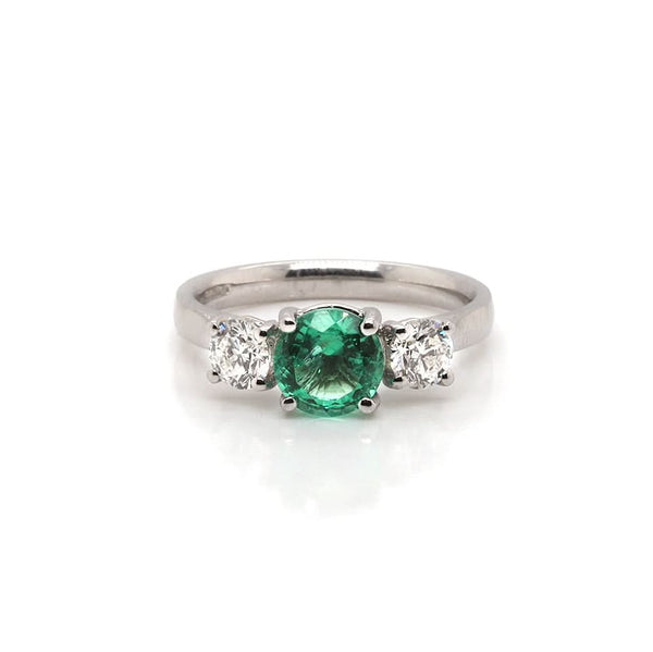 A three stone ring set with an emerald and two diamonds, in platinum