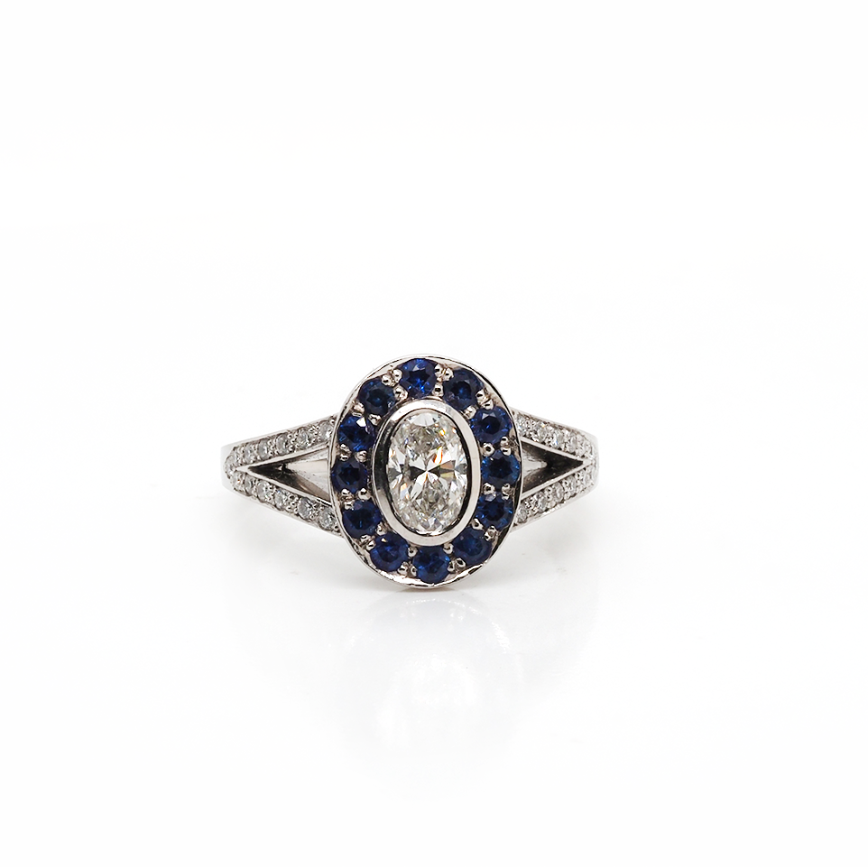 A platinum ring with an oval diamond centre, surrounded by sapphires, with diamond set split shoulders