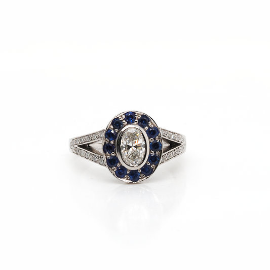 A platinum ring with an oval diamond centre, surrounded by sapphires, with diamond set split shoulders