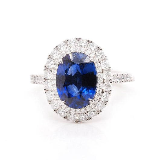 An oval shaped cluster ring with an oval sapphire and a diamond surround, with diamond set shoulders, in platinum