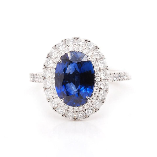 An oval shaped cluster ring with an oval sapphire and a diamond surround, with diamond set shoulders, in platinum
