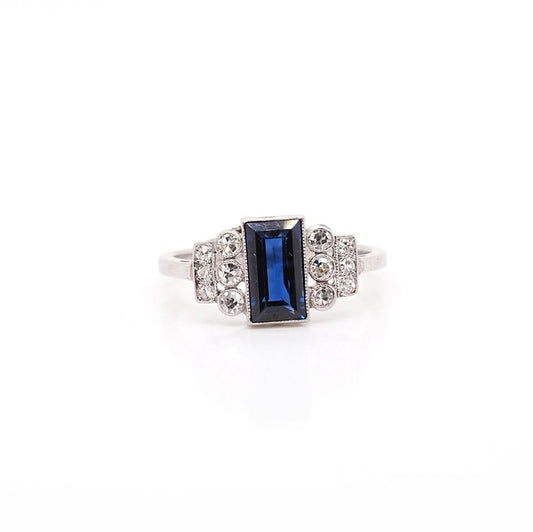 A platinum Art Deco design ring with a central sapphire and diamond set shoulders