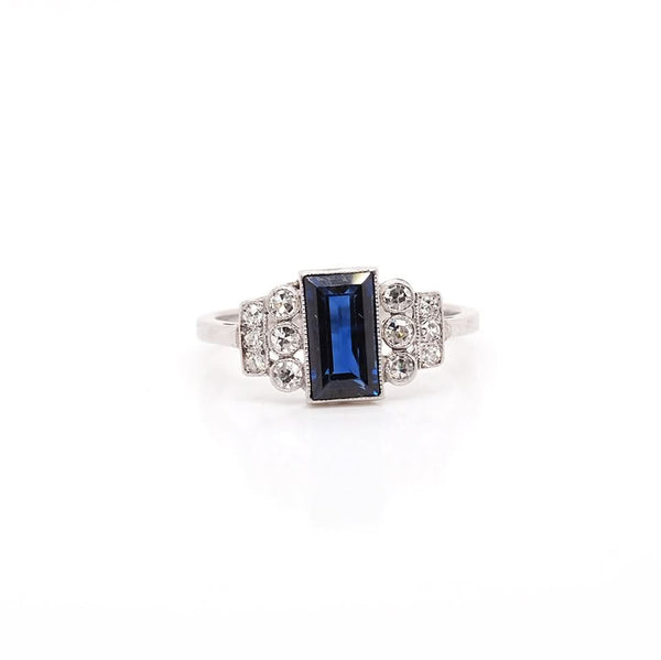A platinum Art Deco design ring with a central sapphire and diamond set shoulders