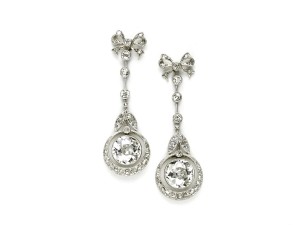 Edwardian diamond drop earrings, with bow tops, three diamonds divided by knife edges, between two diamond set leaves, with a crescent circle, surrounding a pendant old-cut diamond, circa 1900.