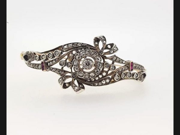 Vintage bangle set with round cut diamonds displaying an intricate floral bow design, finished with two princess cut rubies on either side. Circa 1930's