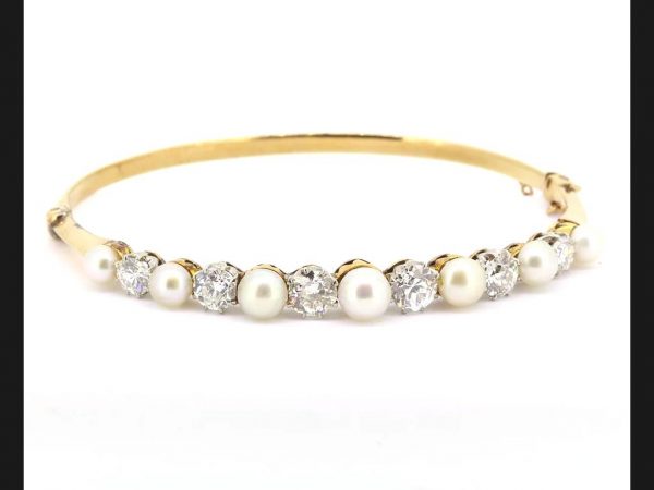 An elegant example of an Edwardian hinged bangle set with natural pearls and diamonds, in 18ct yellow gold a platinum. A beautiful and timeless piece