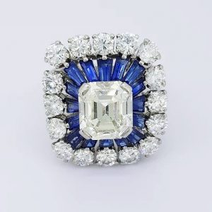 2.30ct Emerald Cut Diamond and Sapphire Cluster Cocktail Ring; 2.30 carat emerald-cut diamond, surrounded by calibre-cut sapphires and 3.00cts diamonds