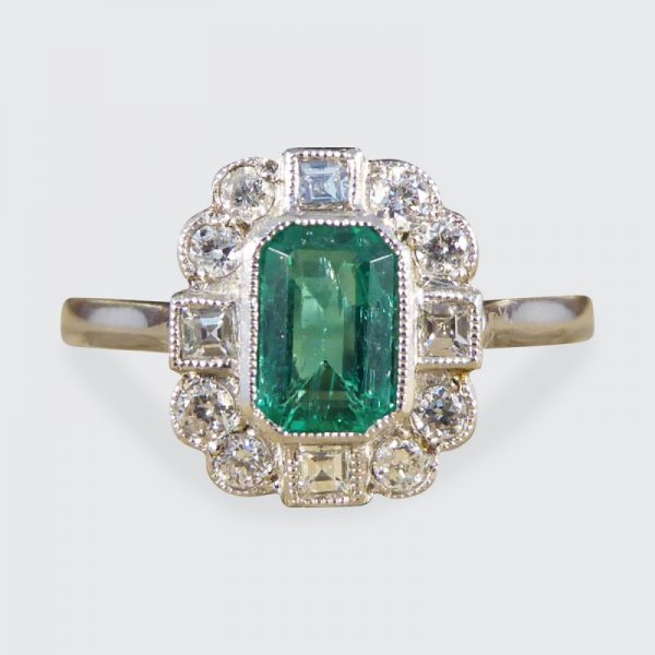 A beautiful contemporary ring featuring a 0.50ct emerald cut emerald with a diamond surround. With princess and modern brilliant cut diamonds alternating around the emerald, this ring has a total of 0.35ct diamonds allowing it to sparkle beautifully on the finger all set in platinum in a millegrain edge.