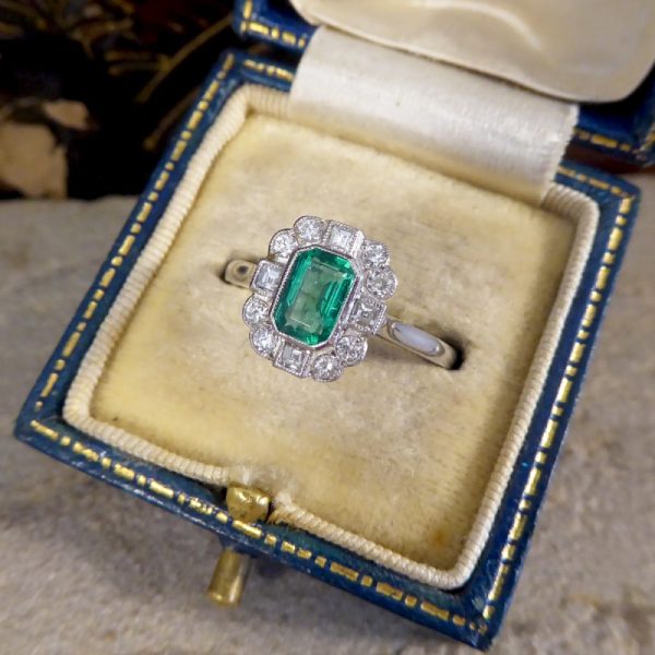A beautiful contemporary ring featuring a 0.50ct emerald cut emerald with a diamond surround. With princess and modern brilliant cut diamonds alternating around the emerald, this ring has a total of 0.35ct diamonds allowing it to sparkle beautifully on the finger all set in platinum in a millegrain edge.