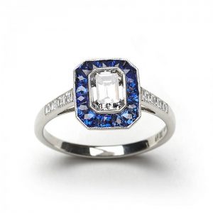 Emerald Cut Diamond and Sapphire Cluster Ring; 0.69ct E VS2 emerald-cut diamond surrounded by calibre-cut sapphires, square-cut diamond set shoulders, mounted in platinum