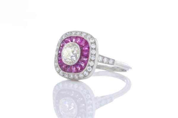 Art Deco Style Old Diamond and Ruby Cluster Target Ring in Platinum; 0.70ct old cut diamond surrounded by baguette cut rubies and an outer halo of old cut diamonds. Accented with diamond set shoulders and a pierced under-gallery.