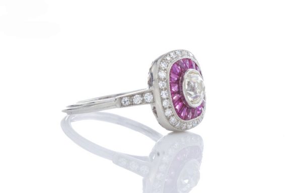 Art Deco Style Old Diamond and Ruby Cluster Target Ring in Platinum; 0.70ct old cut diamond surrounded by baguette cut rubies and an outer halo of old cut diamonds. Accented with diamond set shoulders and a pierced under-gallery.