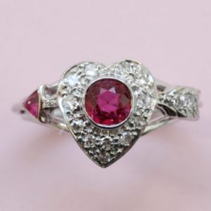 Vintage 1950s Ruby and Diamond Heart and Arrow Ring; 0.75ct round old-cut ruby surrounded by 0.30cts diamonds, in platinum and white gold