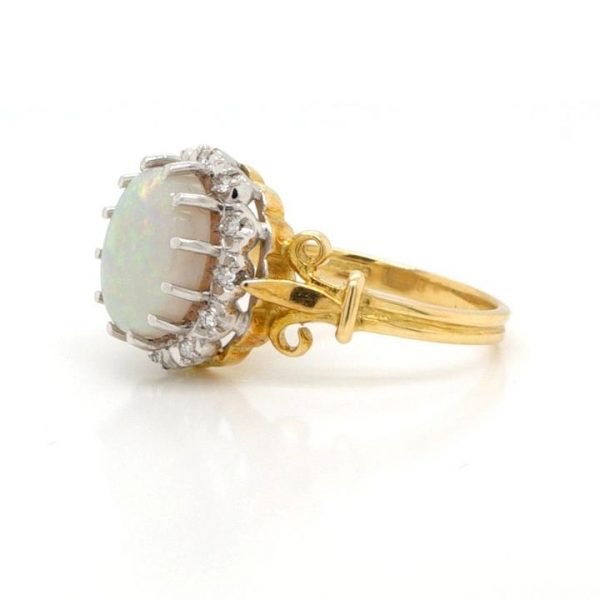 Vintage Opal and Diamond Oval Cluster Ring; featuring a white opal with easily distinguishable flecks in a variety of colours, in 18ct Yellow Gold with scrolled Fleur de Lys shoulders