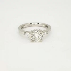 Solitaire Diamond Engagement Ring; featuring a 1.09ct round-cut diamond, four claw set, accented with 0.15cts tapered baguette-cut diamond set shoulders. Mounted in platinum