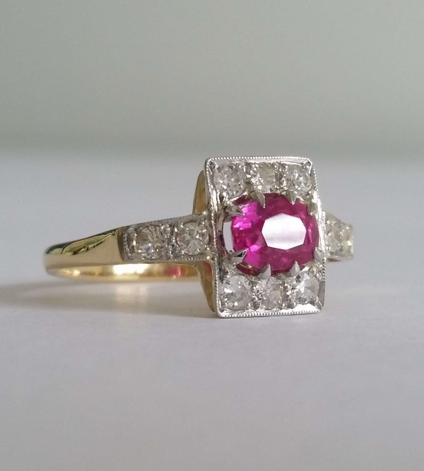 Art Deco Pink Sapphire and Old Cut Diamond Cluster Ring; an oval pink sapphire of intense colour is set in 18ct gold and platinum surrounded by small old cut diamonds. Circa 1920s