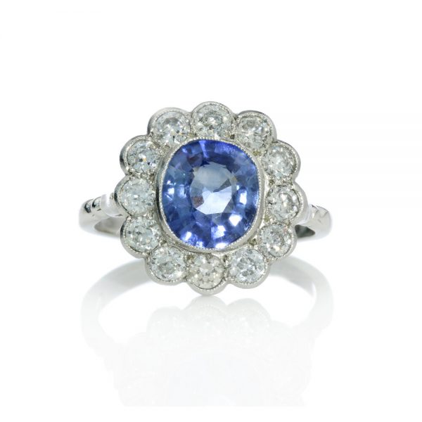 Natural Ceylon Sapphire and Diamond Floral Cluster Ring; featuring a 2 carat oval faceted Natural Ceylon sapphire surrounded by 1.20cts diamonds, in platinum and 18ct white gold