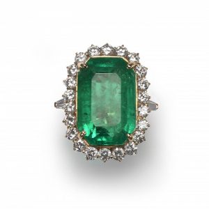 Vintage Colombian Emerald and Diamond Cluster Ring; featuring a central 21.00 carat emerald-cut emerald of Colombian origin, surrounded by twenty-two round brilliant-cut diamonds, 2.20 carat total, in 18ct yellow gold, Circa 1980. Accompanied by a GCS certificate