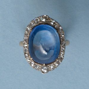 Antique Edwardian Cabochon Cut Sapphire and Diamond Oval Cluster Ring; 16.00 carat oval-cabochon cut sapphire surrounded by rose-cut diamonds, in silver and 18ct yellow gold, Circa 1910