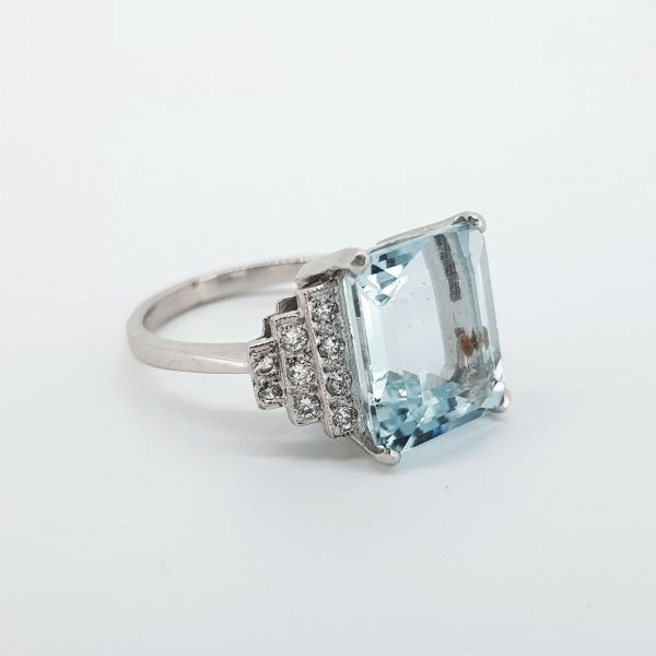 Art Deco Style Aquamarine and Diamond Dress Ring; 5.50ct emerald-cut aquamarine, four-claw set, with 0.85ct diamond set stepped shoulders, in platinum