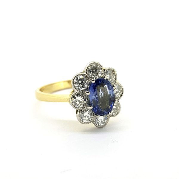 Sapphire and Diamond Floral Cluster Ring; featuring a 1.25ct oval faceted sapphire within a 0.90ct diamond surround, in platinum and 18ct yellow gold