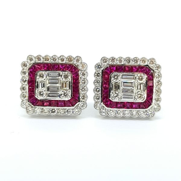Diamond and Ruby Cluster Stud Earrings; central illusion diamond cluster is comprised of baguette and brilliant-cut diamonds, surrounded by a halo of calibre set rubies, and an outer scalloped millegrain edge of round brilliant diamonds, in 18ct white gold