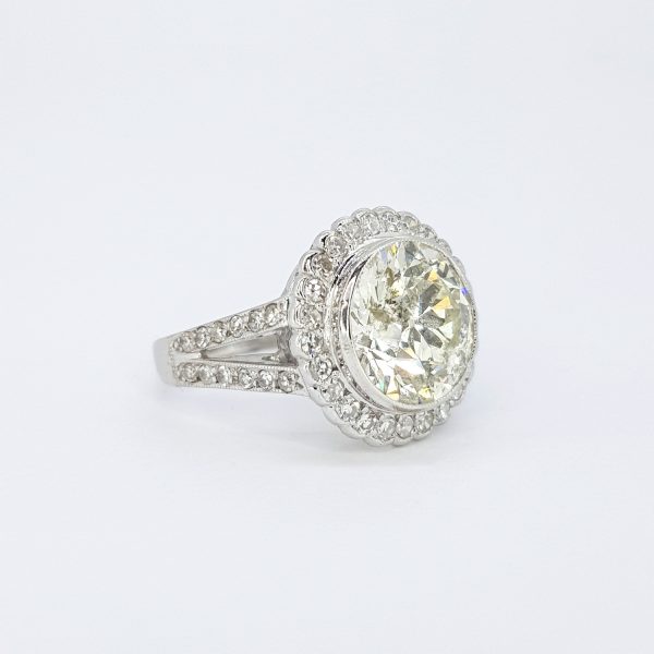 Old Cut Diamond Cluster Cocktail Ring; central 3.67ct round old brilliant-cut diamond surrounded by 0.60cts eight-cut diamonds, bezel set with fluted edge, diamond set split shoulders, in 18ct white gold