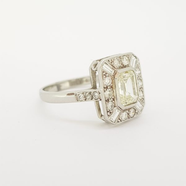 Art Deco Style Emerald Cut Diamond Cluster Ring; central emerald-cut diamond within a surround of brilliant and baguette-cut diamonds, diamond set shoulders, in 18ct white gold